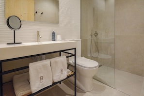 A modern bathroom with a glass-enclosed shower, a white sink with a mirror, and a towel rack with towels. - Bytra Boutique Hotel (Petra)