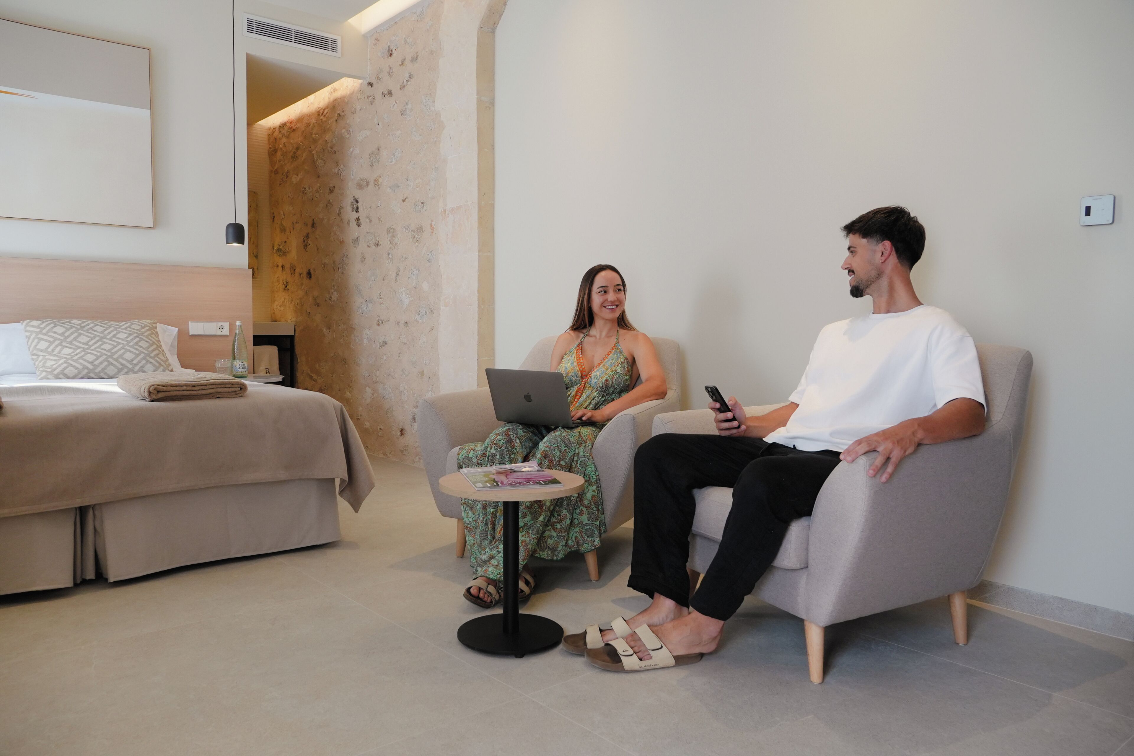 Una habitación de hotel moderna con una cama, una mesita y dos personas sentadas en sillas.