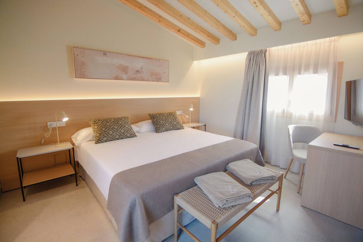 A hotel room with a bed, bedside tables, a desk, a chair, and a television.