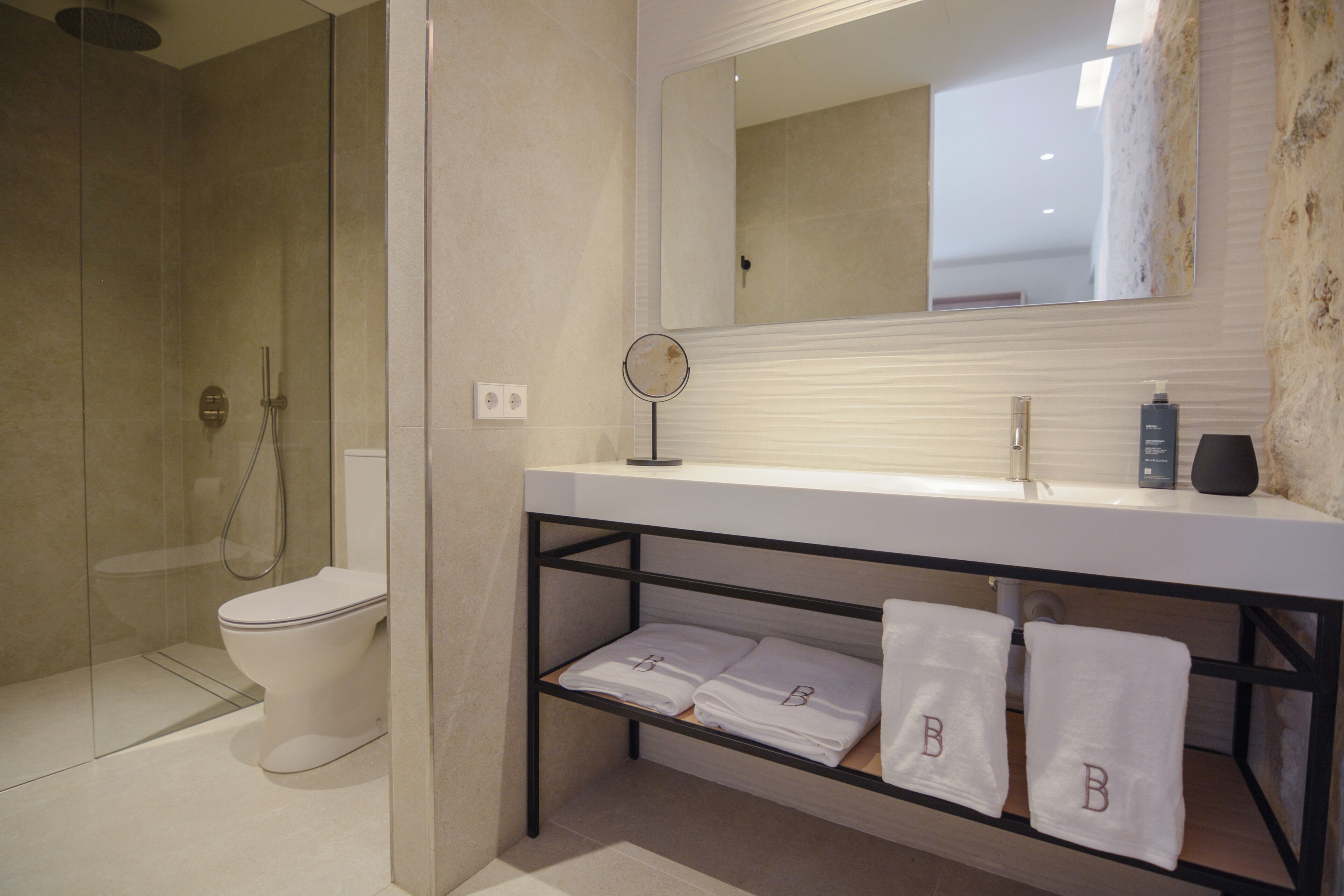 Un baño moderno con ducha envuelta en vidrio, un inodoro, un lavamanos con espejo y un estante con toallas.