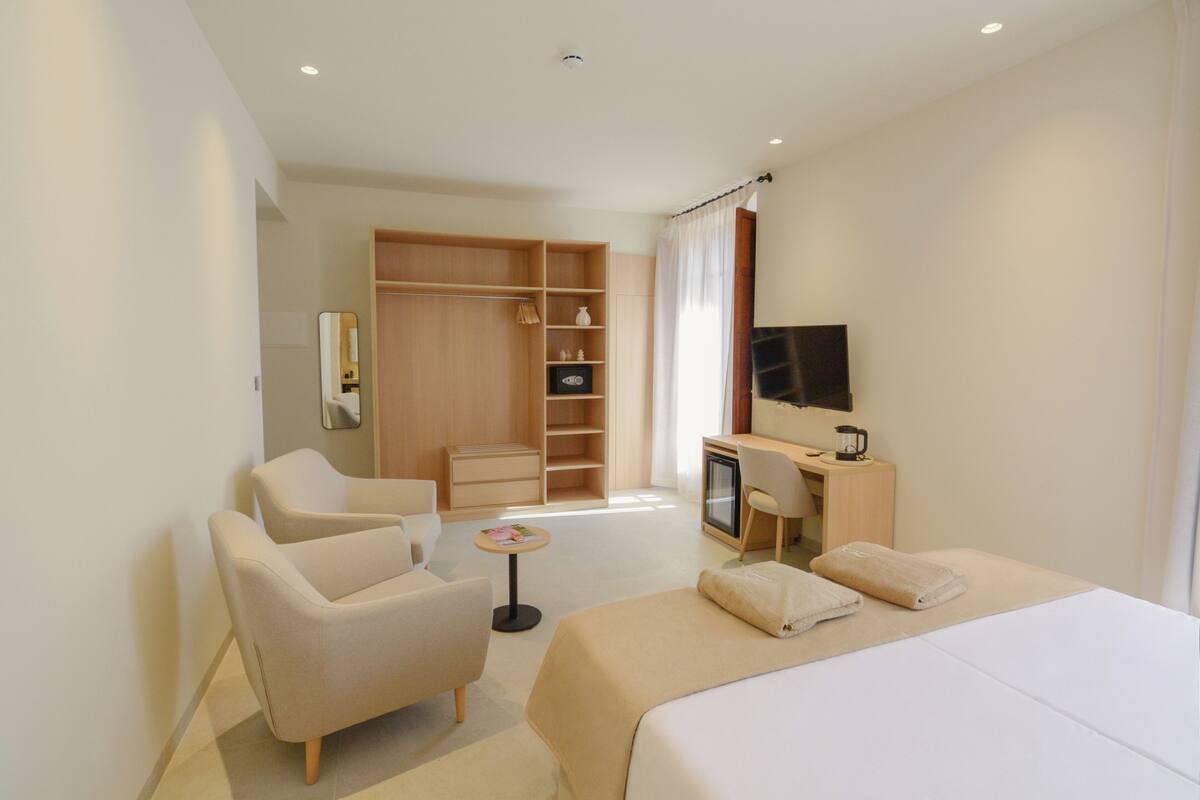 A modern hotel room with a bed, a desk, a chair, a wardrobe, and a television.