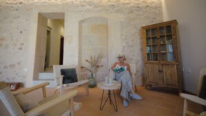 Una habitación con paredes de piedra, un aparador de madera, sillas de mimbre y una mesita con velas.