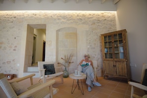 Una habitación con paredes de piedra, un aparador de madera, sillas de mimbre y una mesita con velas.