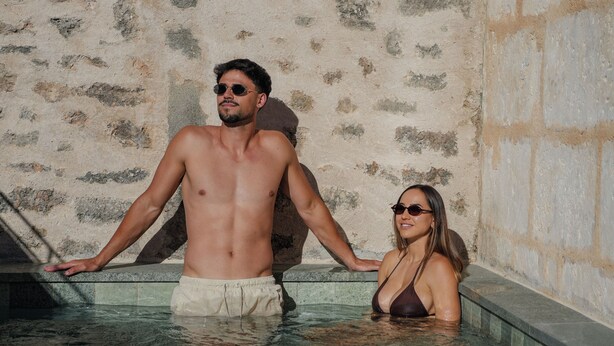 Un homme et une femme dans une piscine dont les murs sont en pierre.