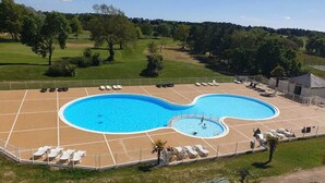Ein Schwimmbecken mit wellenförmigem Design, umgeben von Liegestühlen und einem eingezäunten Bereich.