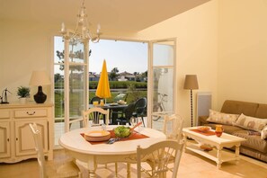 A dining area with a round table, chairs, and a view of the outdoors through large glass doors. - Bon marché ! Maison avec terrasse privée | + Golf (Saint Gilles Croix de Vie)