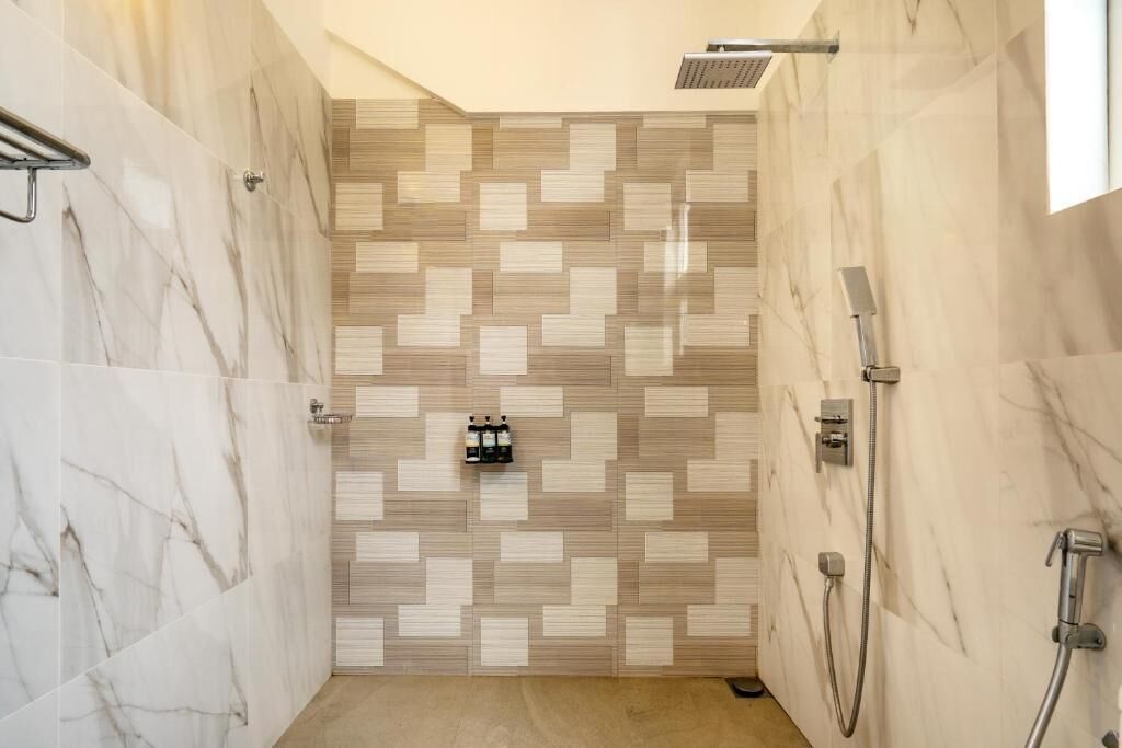 A shower with a tiled wall, a handheld showerhead, and a wall-mounted control panel.