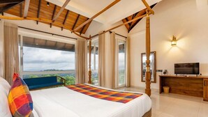 A bedroom with a large bed, a television, a wooden desk, and a balcony with a view.