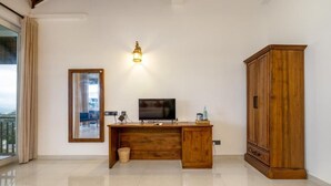 A room with a wooden desk, a television, a mirror, a cabinet, and a window with curtains.