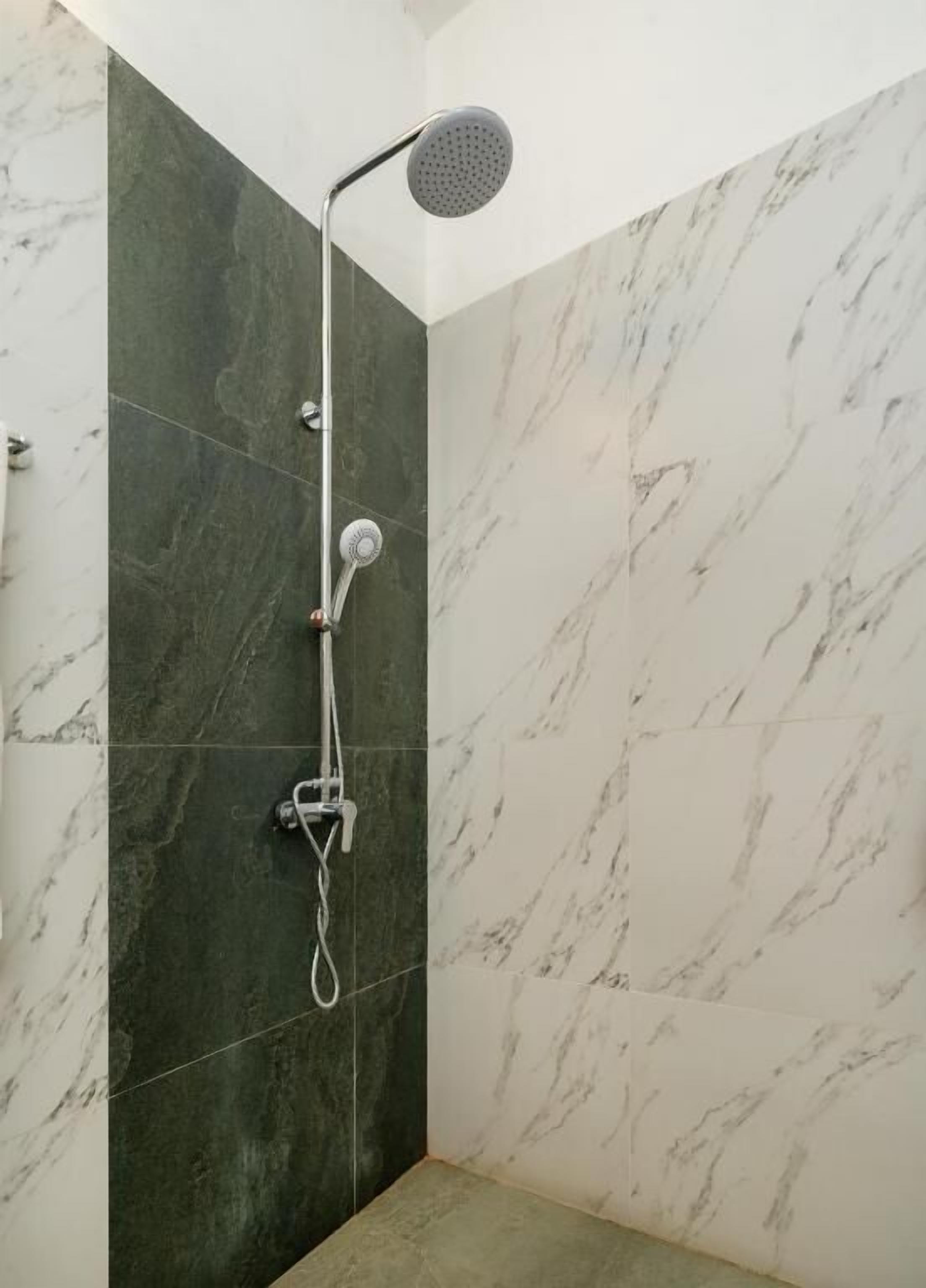 A shower with a handheld showerhead and a wall-mounted faucet, set against a marble wall.