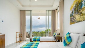 A hotel room with two beds, a balcony with a view, a painting on the wall, and a desk with a lamp.