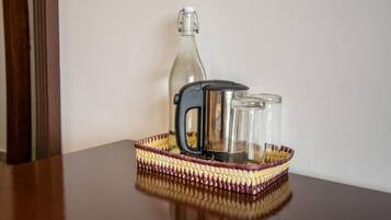 A glass bottle, a kettle, and two glasses on a woven tray on a table.