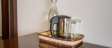 Una botella de vidrio, una tetera y dos vasos sobre una bandeja tejida en una mesa.