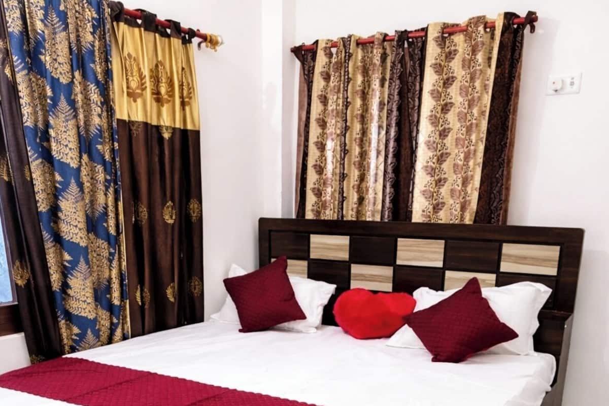 Una cama con estructura de madera, ropa de cama blanca, almohadas rojas y granate, y una manta roja.