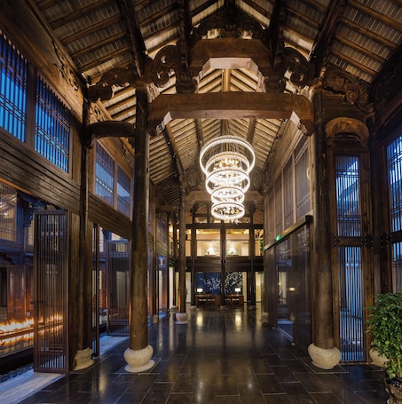 A corridor with wooden columns, a chandelier, and traditional windows.