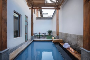 Un área de piscina interior tranquila con un banco de madera, una mesa con sillas y un pequeño jardín.