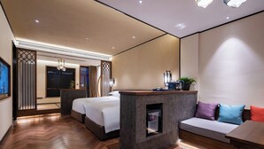 Una habitación de hotel moderna con piso de madera en patrón de espiga, una cama grande, un sofá, un escritorio pequeño y un espejo.