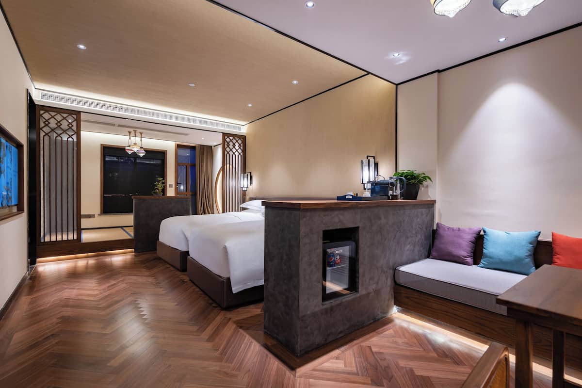 Una habitación de hotel moderna con piso de madera en patrón de espiga, una cama grande, un sofá, un escritorio pequeño y un espejo.