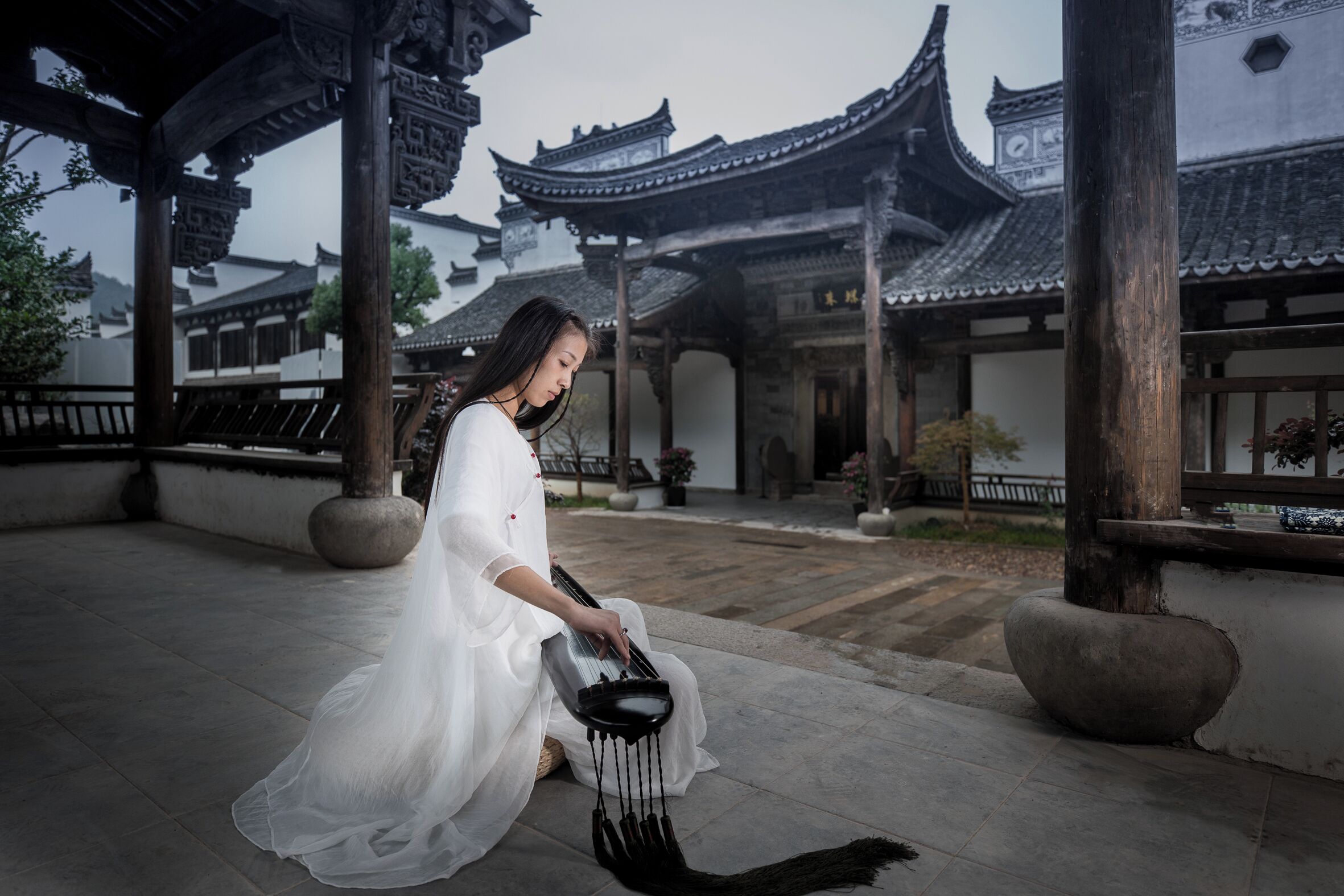 A person playing a traditional stringed instrument in a courtyard with traditional architecture.