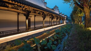 A traditional building with a long corridor, columns, and a waterway with lotus plants. - Deefly Origin House Wuyi (Jinhua)