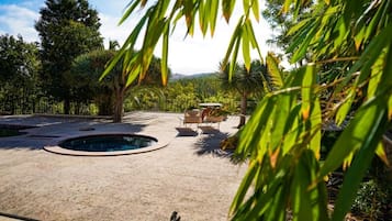 Un espace piscine doté d’un jacuzzi circulaire, entouré de palmiers et offrant une vue sur les collines lointaines.