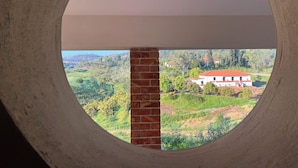 Une fenêtre circulaire donnant sur un mur de briques et un bâtiment blanc avec un toit rouge.