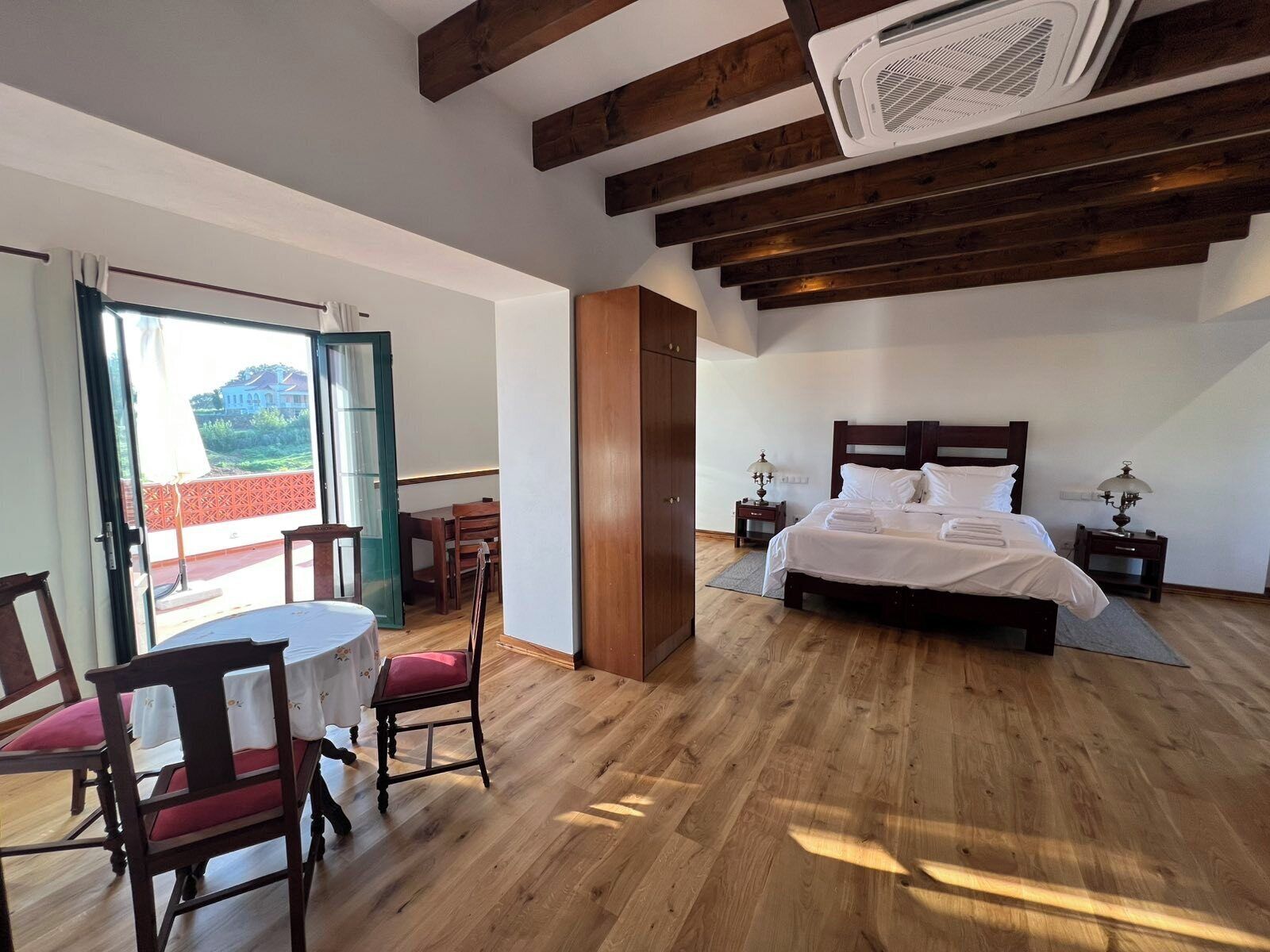 Un dormitorio con cama, mesitas de noche, una mesa con sillas y un balcón con vistas.