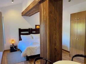 A bedroom with a wooden headboard, a bed with white bedding, a nightstand with a lamp, and a wardrobe.