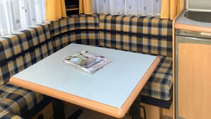 En kompakt campingvogns indretning med spisebord, bænke, et tekøkken og en loftsvifte.