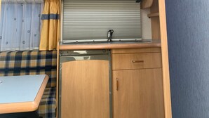 Et kompakt køkken i en autocamper med ovenlys, et spiseområde og en lille vask.