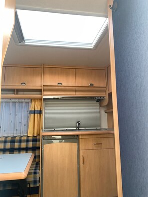 Een compacte RV-keuken met dakraam, een eethoek en een klein spoelbakje.