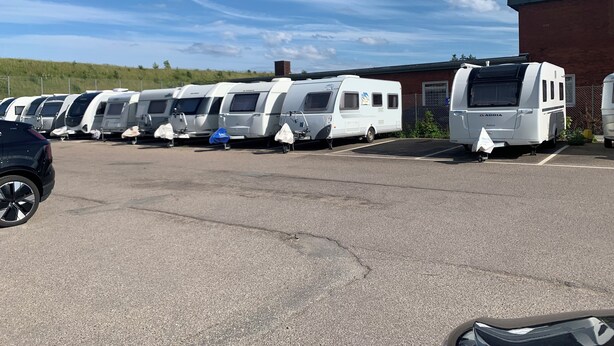En parkeringsplads med flere autocampere parkeret i række, en murstensbygning og en klar himmel.