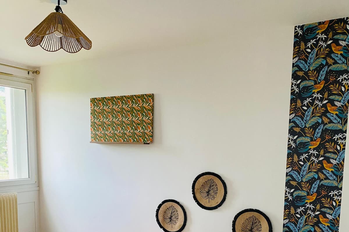 A bedroom with a bed, a hanging light fixture, a wall with decorative leaf patterns, and a window.