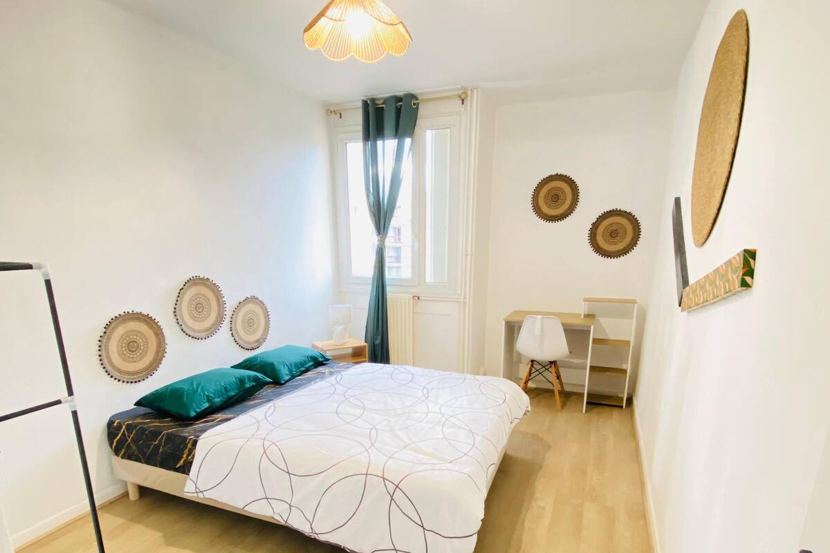 A bedroom with a bed, desk, chair, and a hanging light fixture.