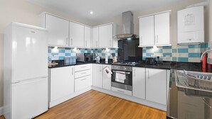 A modern kitchen with white cabinets, a black countertop, a built-in oven, and a dish rack. - Heathrow Living 2BDR 2BA Apt by 360 Stays - Apt 02 (Stanwell)
