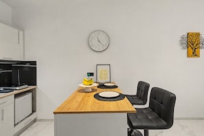 Uma cozinha moderna com uma ilha de madeira, cadeiras pretas, um relógio e um quadro com uma placa de boas-vindas.
