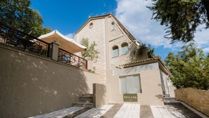 Un bâtiment à la façade en pierre, un escalier menant à une porte portant l’inscription « DOLIVA », et un espace extérieur abrité aménagé en coin salon.