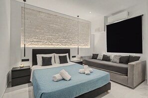 Une chambre moderne avec un grand lit, un canapé gris, un téléviseur à écran plat et un mur à la texture de pierre.