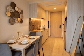 Une cuisine moderne avec un plan de travail en marbre, un coin repas avec une table dressée pour deux personnes, et un couloir menant à une porte.