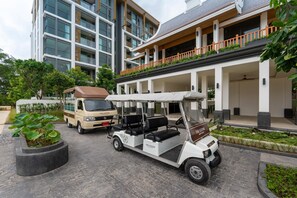 Un carrito de golf estacionado frente a un edificio con un espacio al aire libre techado y una camioneta al fondo.