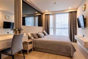Une chambre d’hôtel moderne équipée d’un lit, d’un bureau, d’une chaise, d’une télévision et d’une grande fenêtre avec des rideaux.