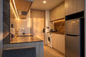Eine moderne Küche mit Holzausstattung, einem Edelstahlkühlschrank, einer integrierten Waschmaschine und einer Arbeitsplatte mit Kaffeemaschine.