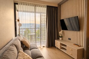 Ein modernes Wohnzimmer mit einer Couch, einem an der Wand befestigten Fernseher und einem Balkon mit Blick.