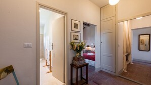 A hallway with a door leading to a bedroom, a small table with a vase, and a mirror on the wall. - Villa Molamezza by MMega (Mercatale in Val di Pesa)