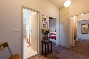 A hallway with a door leading to a bedroom, a small table with a vase, and a mirror on the wall. - Villa Molamezza by MMega (Mercatale in Val di Pesa)