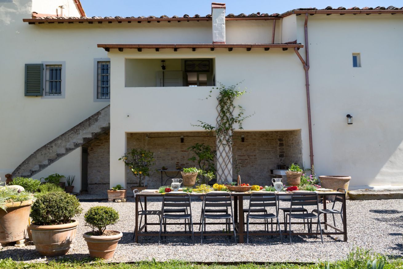 An outdoor dining area with a table set for four, surrounded by potted plants and a stone wall.