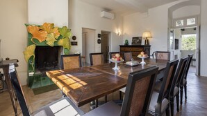 A dining room with a large wooden table, chairs, a fireplace with decorative tiles, and a view of the outdoors. - Villa Molamezza by MMega (Mercatale in Val di Pesa)