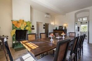 A dining room with a large wooden table, chairs, a fireplace with decorative tiles, and a view of the outdoors. - Villa Molamezza by MMega (Mercatale in Val di Pesa)