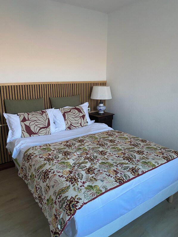 A bed with a floral bedspread, two pillows, a wooden headboard, and a bedside table with a lamp. - Cozy Studio (Avignon)