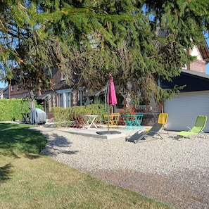 Un patio con mobiliario exterior, una parrilla y un árbol grande que proporciona sombra.
